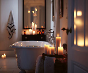Ein stilvolles Badezimmer im Abendlicht, dekoriert mit vielen warm leuchtenden Kerzen. Ein Entspannungsbad am Abend für guten Schlaf.